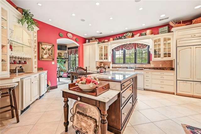 kitchen with cream cabinetry, arched walkways, light tile patterned floors, recessed lighting, and glass insert cabinets