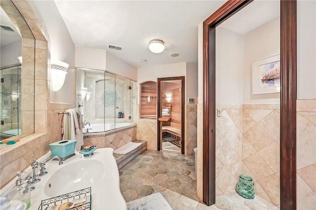 bathroom featuring tile walls, a relaxing tiled tub, a tile shower, a wainscoted wall, and a sink