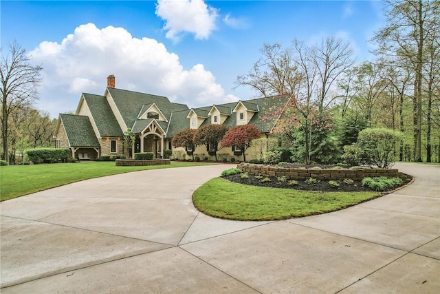 english style home with curved driveway, a front yard, a chimney, and stone siding