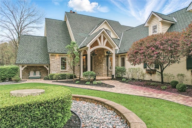 english style home with stone siding, a front lawn, and a high end roof