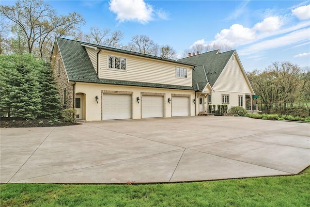 view of side of home with driveway, an attached garage, stucco siding, and roof with shingles