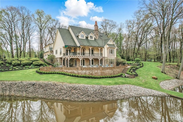 rear view of property featuring a balcony, a chimney, a yard, and a water view