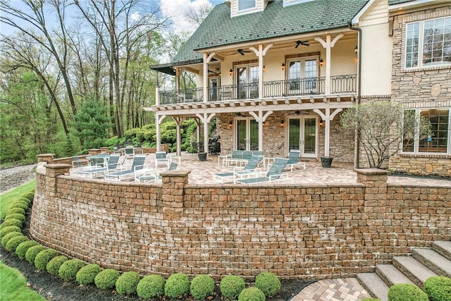 rear view of property featuring french doors, a balcony, ceiling fan, stucco siding, and a high end roof