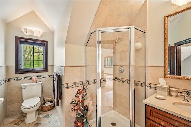 bathroom with tile walls, a shower stall, vanity, vaulted ceiling, and toilet