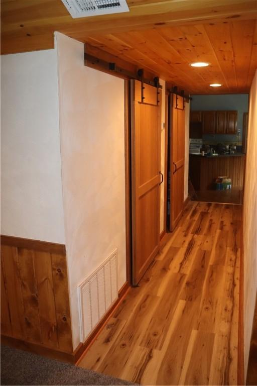 hall featuring a barn door, wooden ceiling, and light wood-style floors