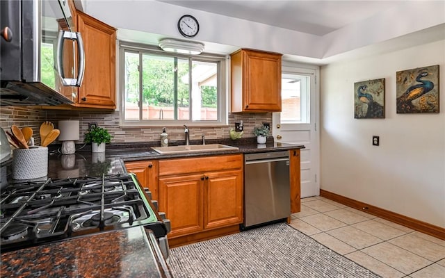 kitchen featuring appliances with stainless steel finishes, a sink, decorative backsplash, and brown cabinetry