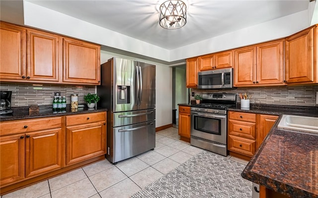 kitchen featuring appliances with stainless steel finishes, light tile patterned floors, brown cabinetry, and decorative backsplash