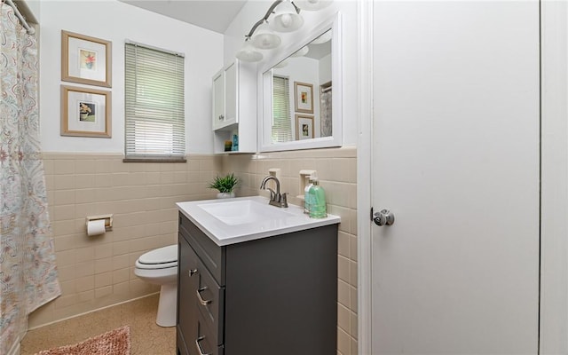 bathroom with tile walls, vanity, toilet, and wainscoting