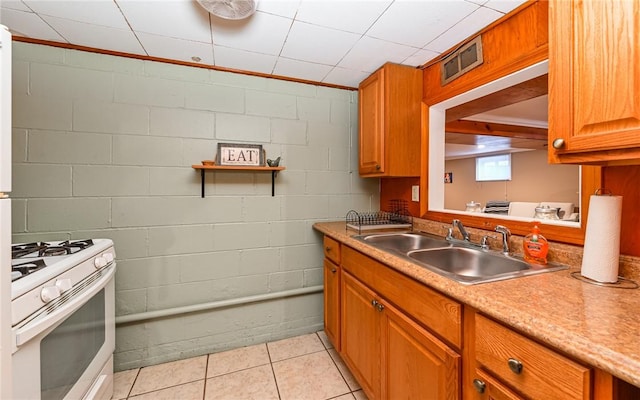 kitchen featuring gas range gas stove, a sink, light countertops, and brown cabinetry