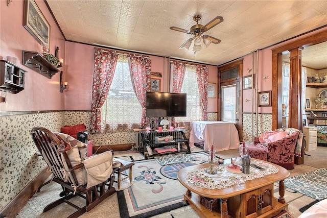 living area with a ceiling fan, wallpapered walls, carpet flooring, and decorative columns