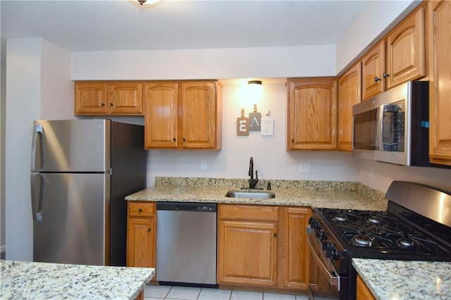 kitchen featuring stainless steel appliances, a sink, light stone counters, and brown cabinets
