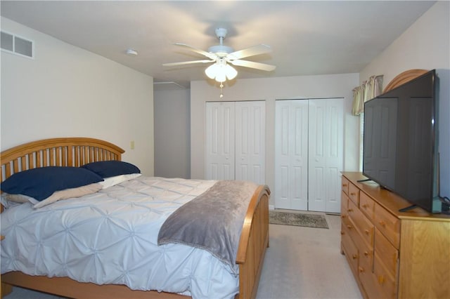 bedroom with two closets, light carpet, and a ceiling fan