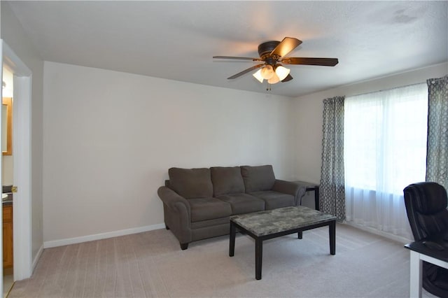 living area with a ceiling fan, light colored carpet, and baseboards