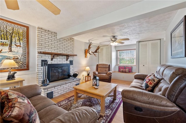 3 Patricia St, Fallowfield, PA 15022 - living room featuring a textured ceiling, ceiling fan, light wood-style flooring, a brick fireplace, and a wainscoted wall