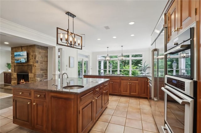 kitchen featuring a sink, a chandelier, brown cabinets, light tile patterned floors, and a kitchen island with sink