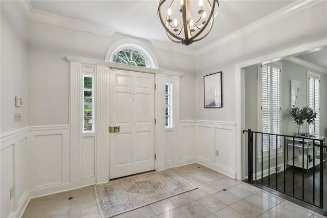 foyer entrance with a decorative wall, a chandelier, light tile patterned floors, ornamental molding, and wainscoting