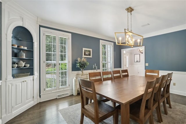 dining space featuring crown molding, a chandelier, dark wood finished floors, and a wainscoted wall