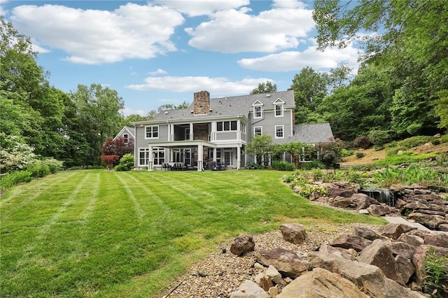 back of property with a sunroom, a chimney, and a yard