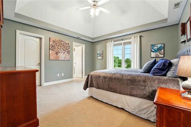 bedroom featuring light carpet, a tray ceiling, baseboards, ceiling fan, and ensuite bath