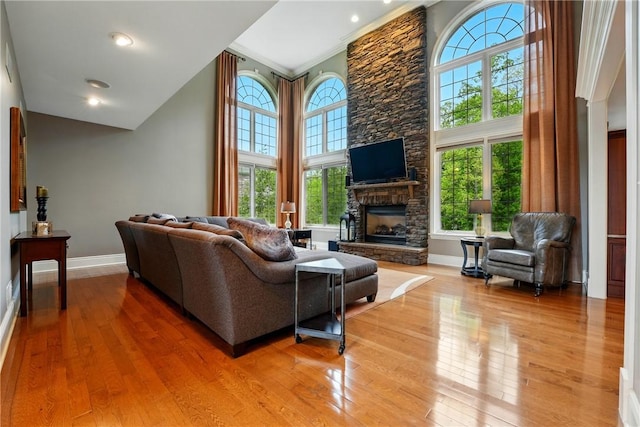 living area with hardwood / wood-style flooring, baseboards, a fireplace, a high ceiling, and ornamental molding