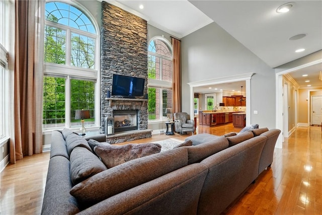 living area featuring high vaulted ceiling, plenty of natural light, a stone fireplace, light wood-style flooring, and baseboards