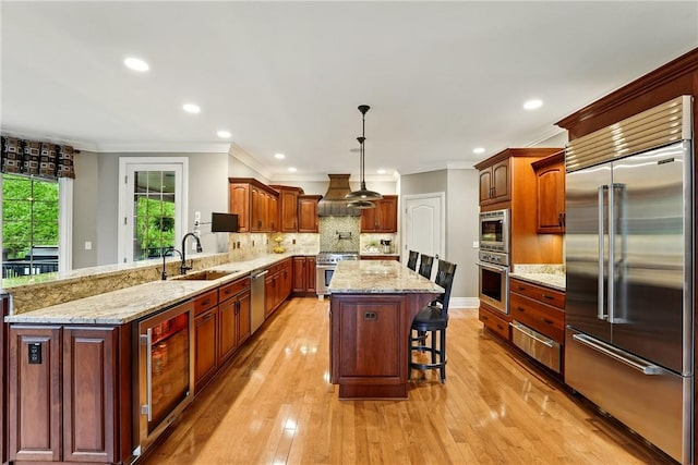 kitchen with built in appliances, a sink, crown molding, beverage cooler, and a kitchen breakfast bar