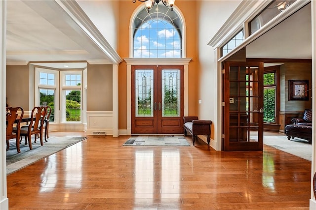 foyer entrance featuring french doors, hardwood / wood-style flooring, crown molding, a chandelier, and wainscoting
