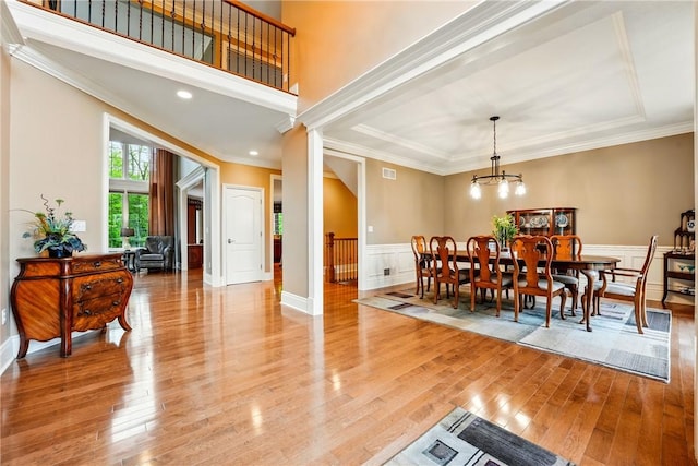 dining area with light wood-type flooring, wainscoting, a chandelier, crown molding, and a decorative wall