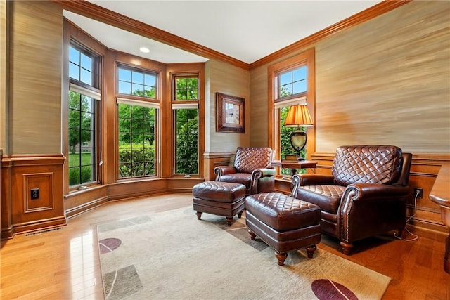 living area with crown molding, wood finished floors, a wainscoted wall, and a decorative wall