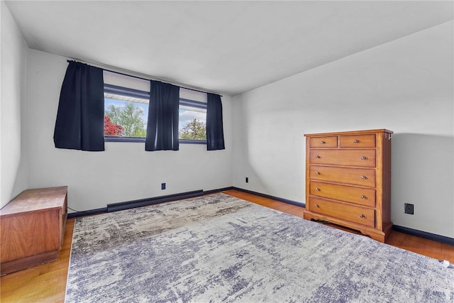 bedroom with wood finished floors, baseboard heating, and baseboards