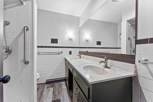 bathroom with tile walls, wood finished floors, double vanity, a wainscoted wall, and a shower