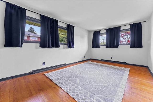 unfurnished room featuring a baseboard heating unit, wood finished floors, and baseboards