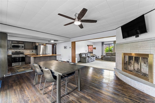dining area with ceiling fan, dark wood-style flooring, and a fireplace