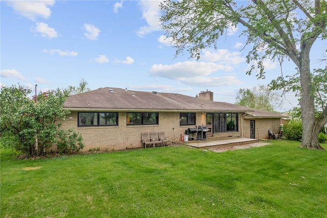 rear view of house featuring a lawn, a chimney, brick siding, and a patio area