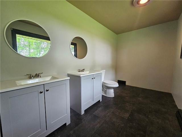 bathroom featuring two vanities, toilet, lofted ceiling, and stone finish floors