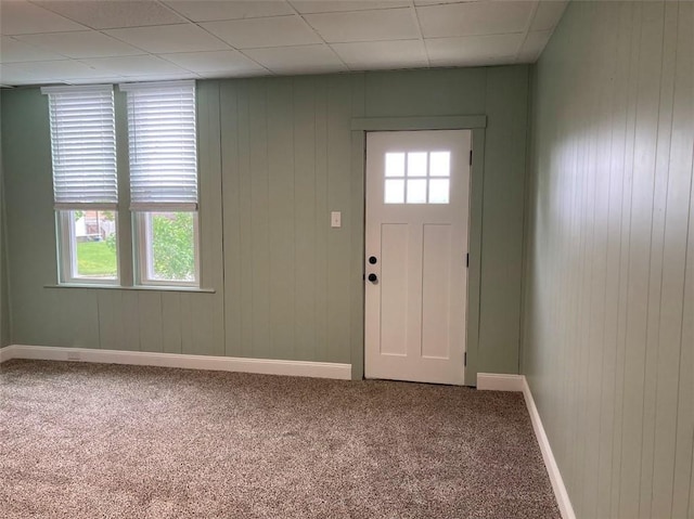 entryway featuring carpet, baseboards, wood walls, and a paneled ceiling