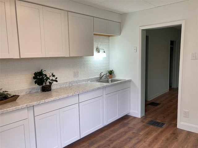 kitchen with a sink, tasteful backsplash, dark wood-style flooring, white cabinetry, and baseboards