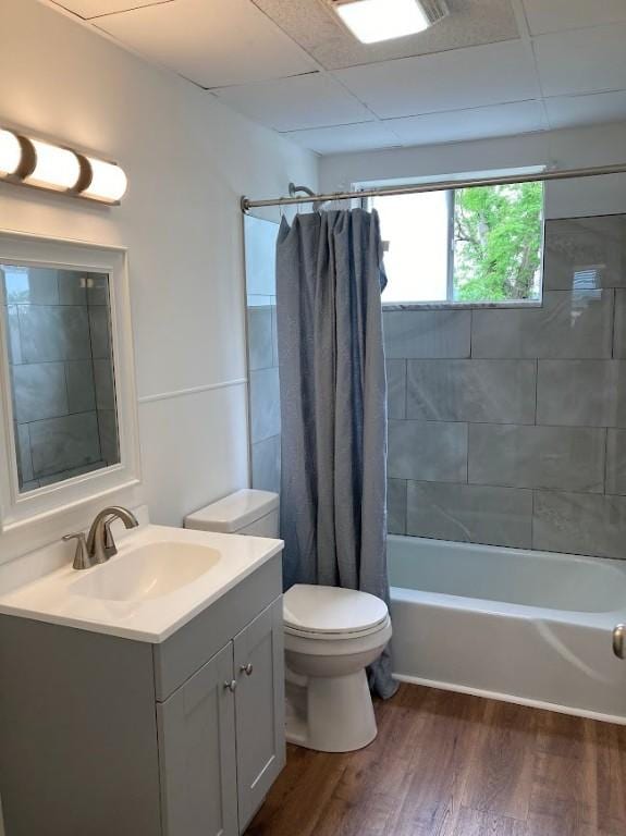 full bathroom featuring wood finished floors, shower / tub combo, toilet, vanity, and a drop ceiling