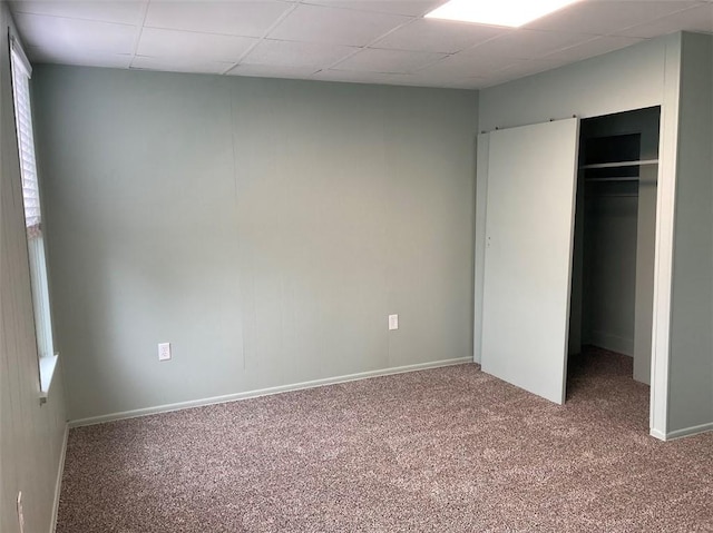 unfurnished bedroom featuring carpet flooring, a drop ceiling, baseboards, and a closet