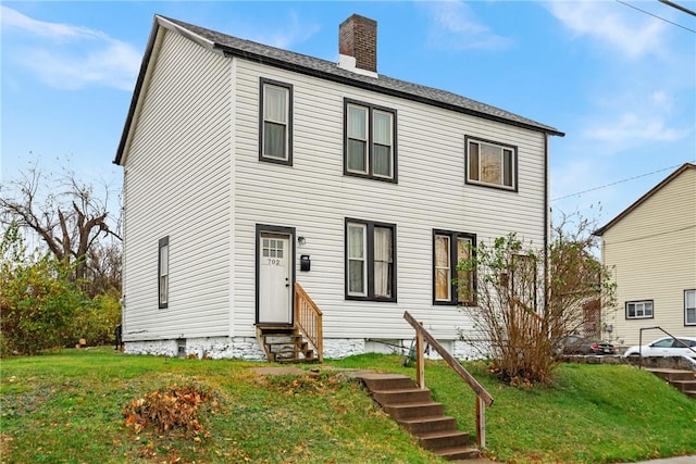 view of front of house featuring entry steps, a chimney, and a front yard