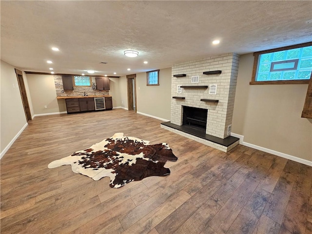 living area with recessed lighting, light wood-type flooring, a fireplace, baseboards, and a textured ceiling