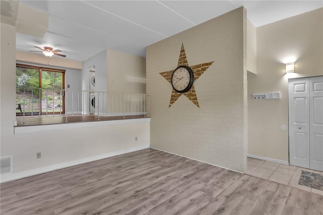 empty room with estacked washer and dryer, wood finished floors, a ceiling fan, baseboards, and brick wall