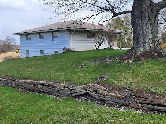 view of side of home featuring a chimney, a yard, and a shingled roof