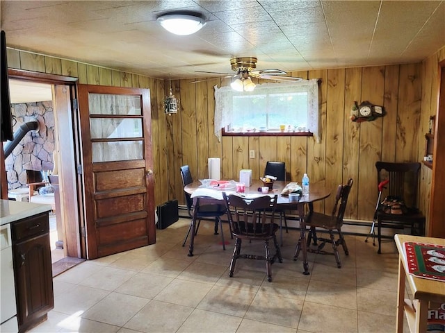 dining room featuring a ceiling fan, wood walls, light tile patterned floors, and a wood stove