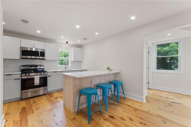 23 Saint Thomas St, South Side, PA 15203 - kitchen with stainless steel appliances, a kitchen bar, light countertops, backsplash, and light wood-type flooring