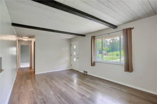 empty room featuring wood finished floors, beamed ceiling, and baseboards