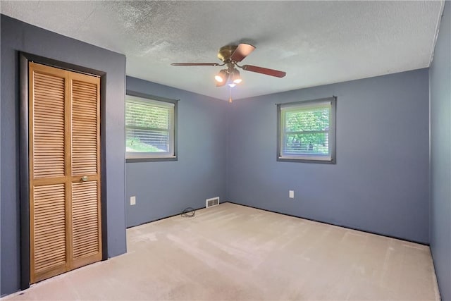 unfurnished bedroom featuring a closet, multiple windows, carpet, a textured ceiling, and a ceiling fan