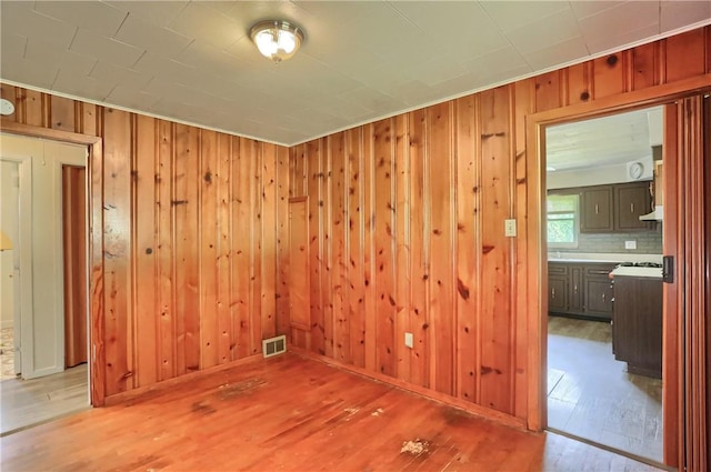 unfurnished room featuring light wood finished floors, wood walls, and crown molding