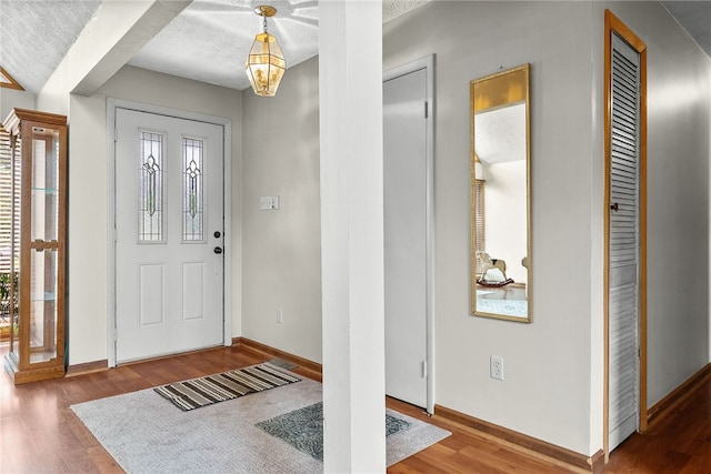 foyer featuring wood finished floors, baseboards, and a textured ceiling