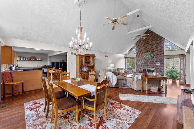 dining area with a ceiling fan, a textured ceiling, wood finished floors, a brick fireplace, and high vaulted ceiling